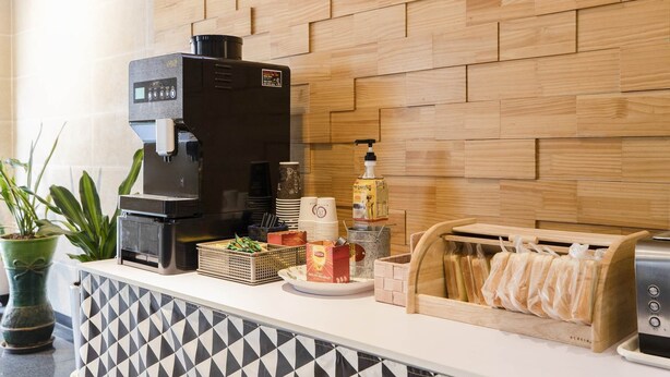 A coffee station with a coffee machine, disposable cups, a syrup dispenser, and a bread toaster. - Hotel Nuri (Osan)