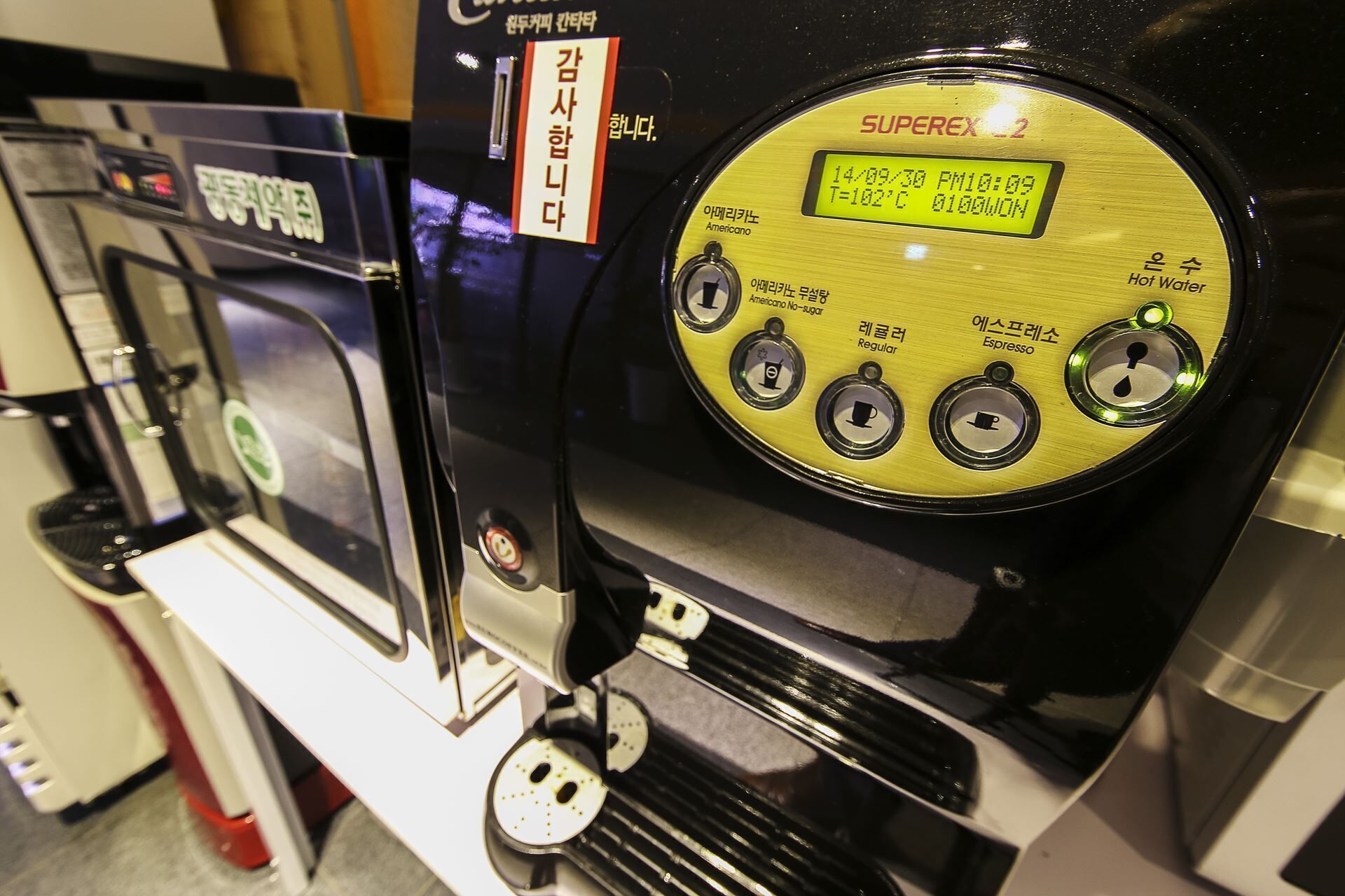 Una cafetera con pantalla digital, diversas opciones de café y un dispensador de agua caliente.
