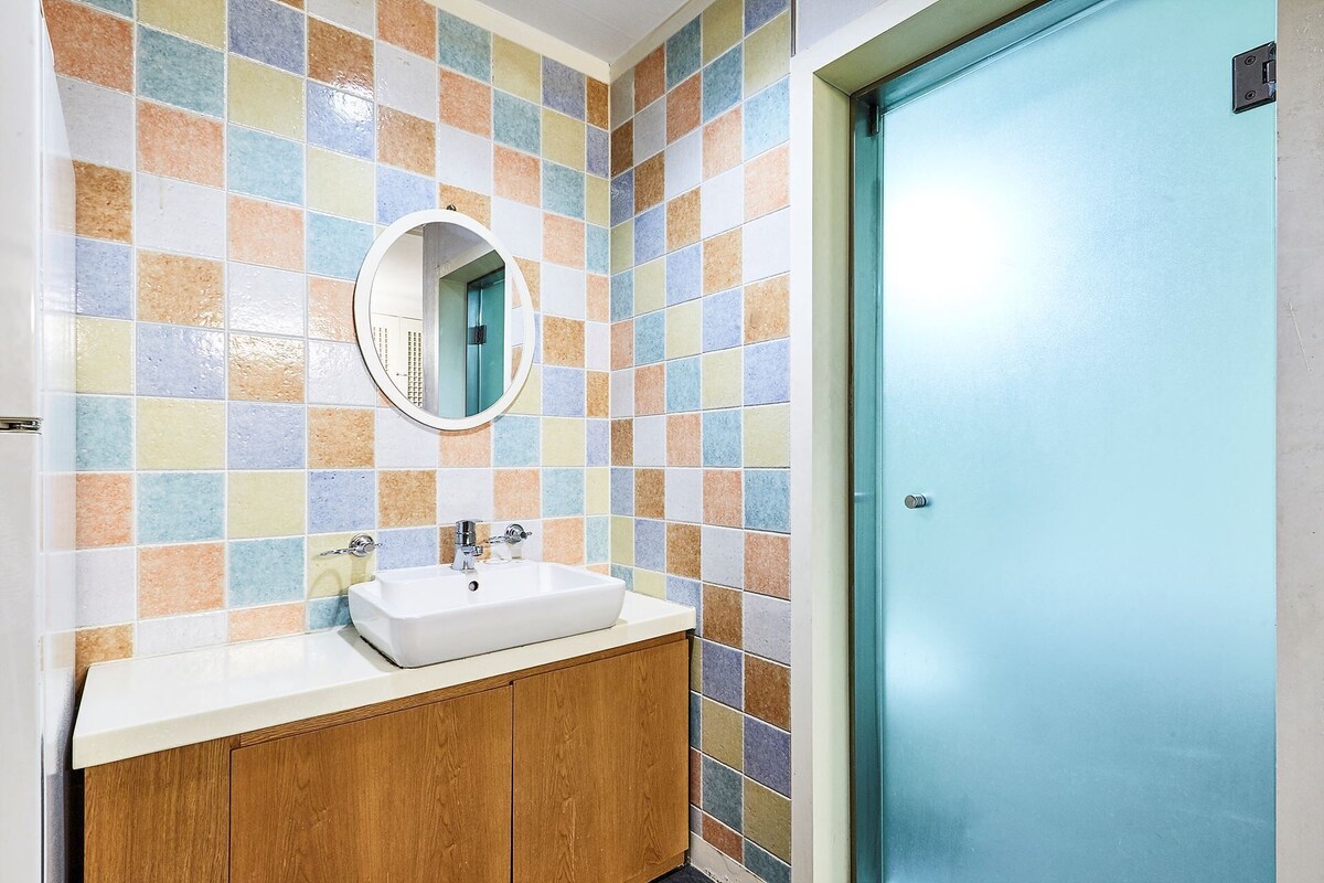 Un baño con pared de azulejos, un lavabo, un espejo y una puerta.