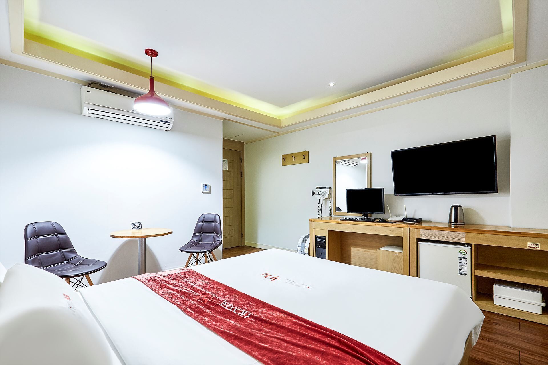 Una habitación de hotel con una cama, dos sillas, un escritorio con una computadora, un televisor y un aire acondicionado.