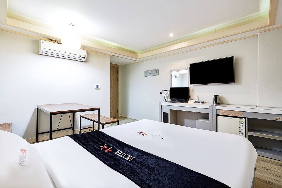 A hotel room with a bed, a desk, a chair, a TV, and an air conditioning unit.