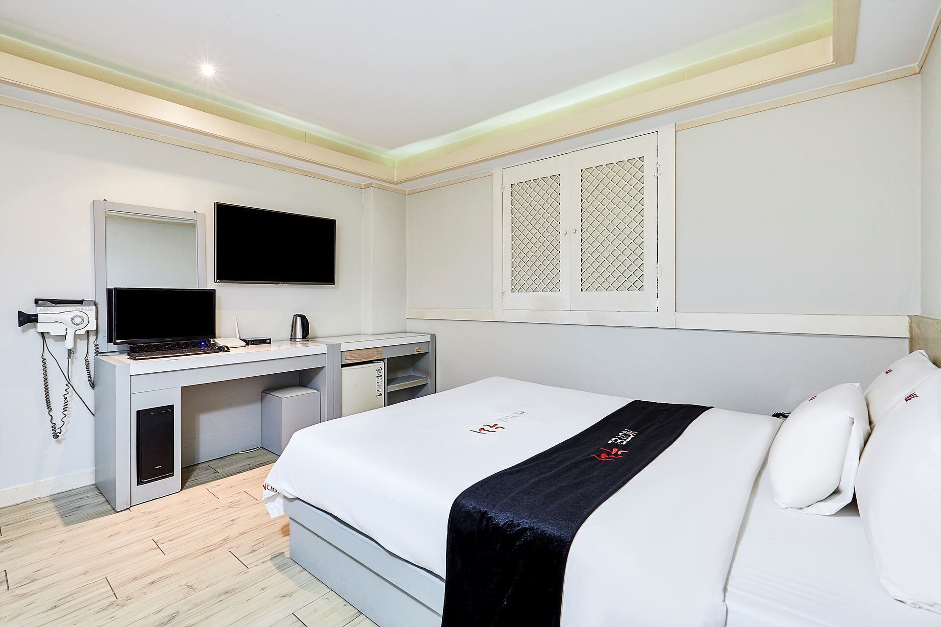 A hotel room with a bed, a desk, a TV, and a minibar.