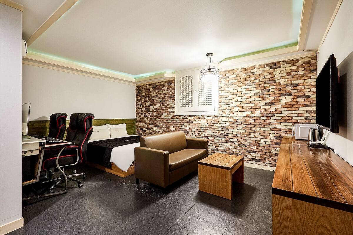 A compact hotel room with a bed, a desk, a chair, a small table, and a TV.