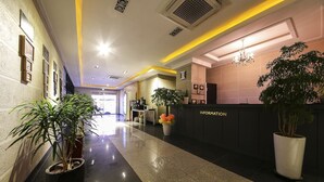 A hotel reception area with a reception desk, a clock, and a potted plant. - Hotel Nuri (Osan)