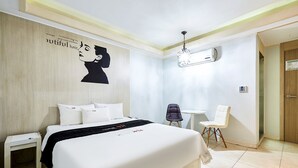 A hotel room with a large bed, a bedside table, a chair, a small table, and an air conditioning unit. - Hotel Nuri (Osan)