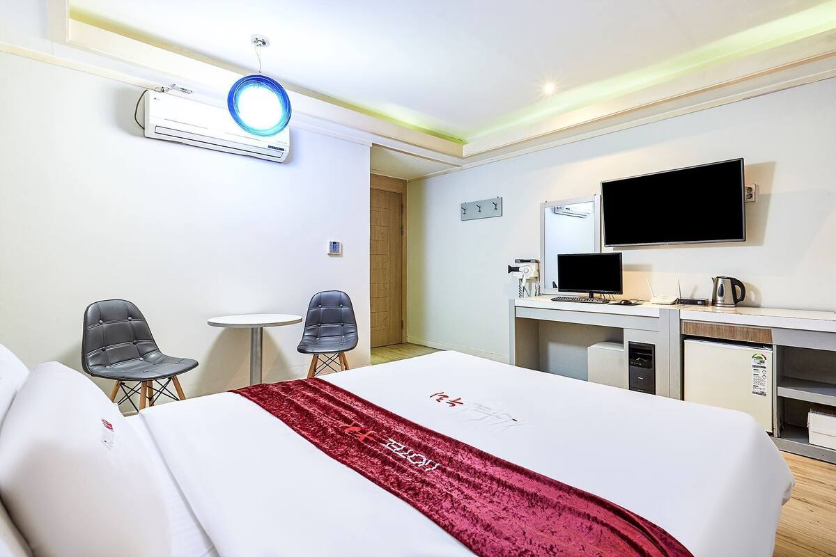 A hotel room with a bed, a desk with a computer, a TV, and a hairdryer.