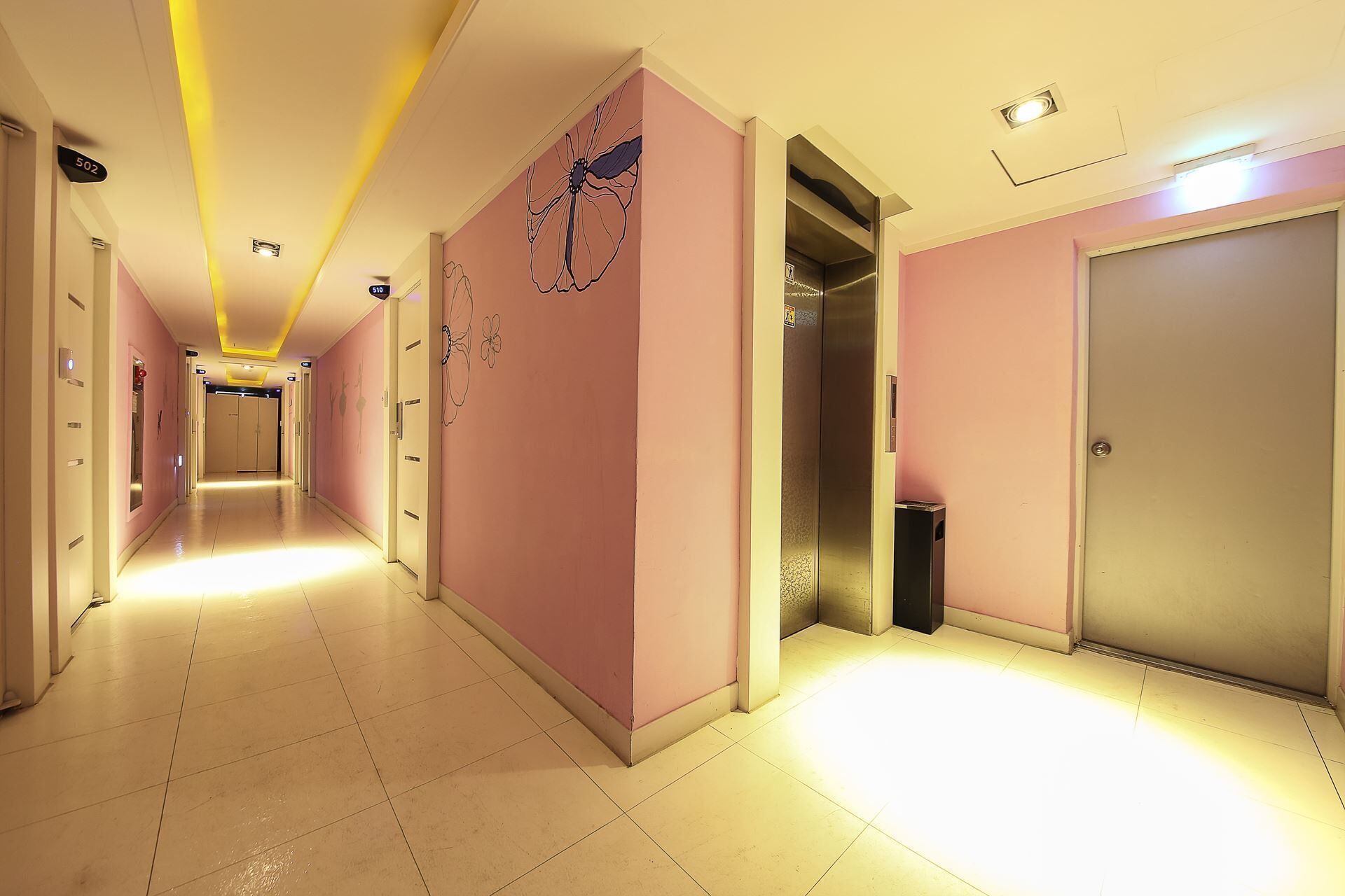 A hotel corridor with pink walls, a tiled floor, and doors leading to rooms.
