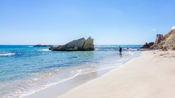 A beach with clear water, a large rock formation, and a person walking. - Modern Town Villa "Bona Mar" with Pool (cala ratjada)