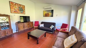 Un salon comprenant un canapé, des fauteuils, une table basse, un téléviseur posé sur un meuble en bois, et des œuvres d’art accrochées aux murs.
