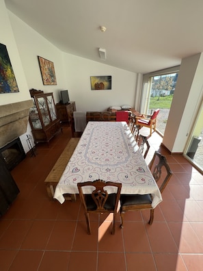 Un espace repas comprenant une longue table, des chaises, une cheminée et une vue à travers une porte vitrée.