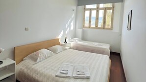 Une chambre d’hôtel avec un grand lit, un lit plus petit, une table de chevet, un bureau et une fenêtre donnant sur un beau paysage.