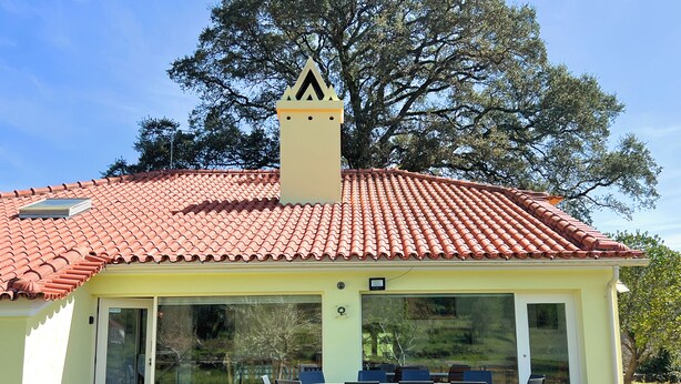 Une maison avec un toit recouvert de tuiles rouges, une cheminée et un patio abrité avec des meubles d’extérieur.