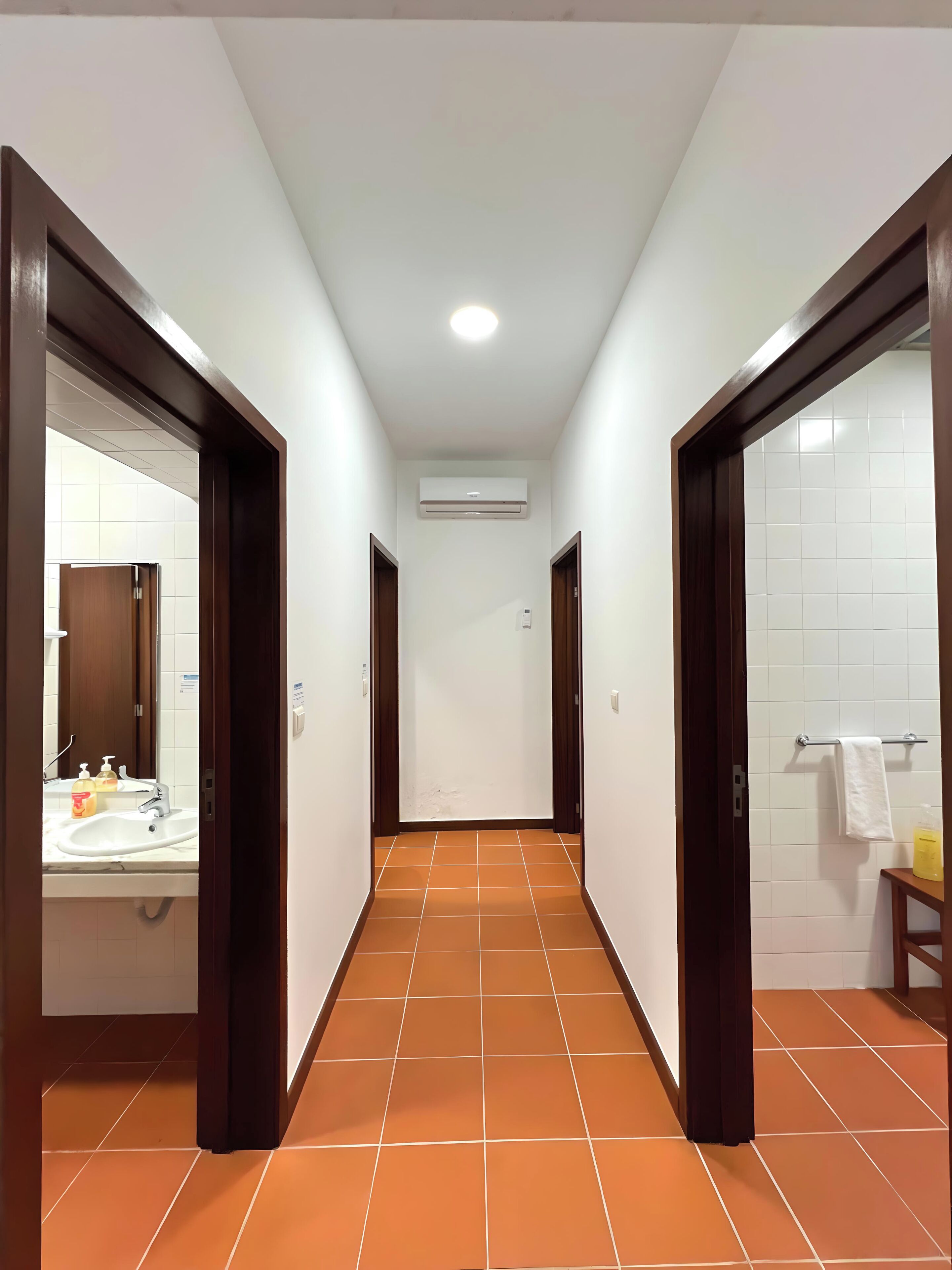 A corridor with a tiled floor, white walls, and wooden doors.