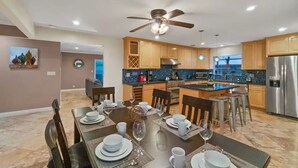 A modern kitchen with wooden cabinets, a stainless steel refrigerator, and a dining area set for six. - *Reduced Pricing* Spacious Disney Vacation w/ Game Room (Orange)