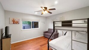 A room with a bunk bed, a sofa, a television, a ceiling fan, and a window with a view of greenery. - *Reduced Pricing* Spacious Disney Vacation w/ Game Room (Orange)