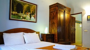 Una habitación de hotel con cama, un armario de madera, un cuadro en la pared y un baño visible a través de una puerta abierta.