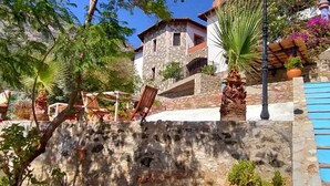 Un edificio de piedra con una escalera que conduce a una zona de piscina, rodeado de vegetación y un cielo despejado.