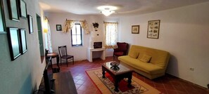 Un salon comprenant un canapé, une table à manger, des chaises, une cheminée et une fenêtre avec des rideaux.