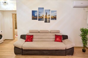 Een woonkamer met een bank, een wandairconditioner en een kamerplant.