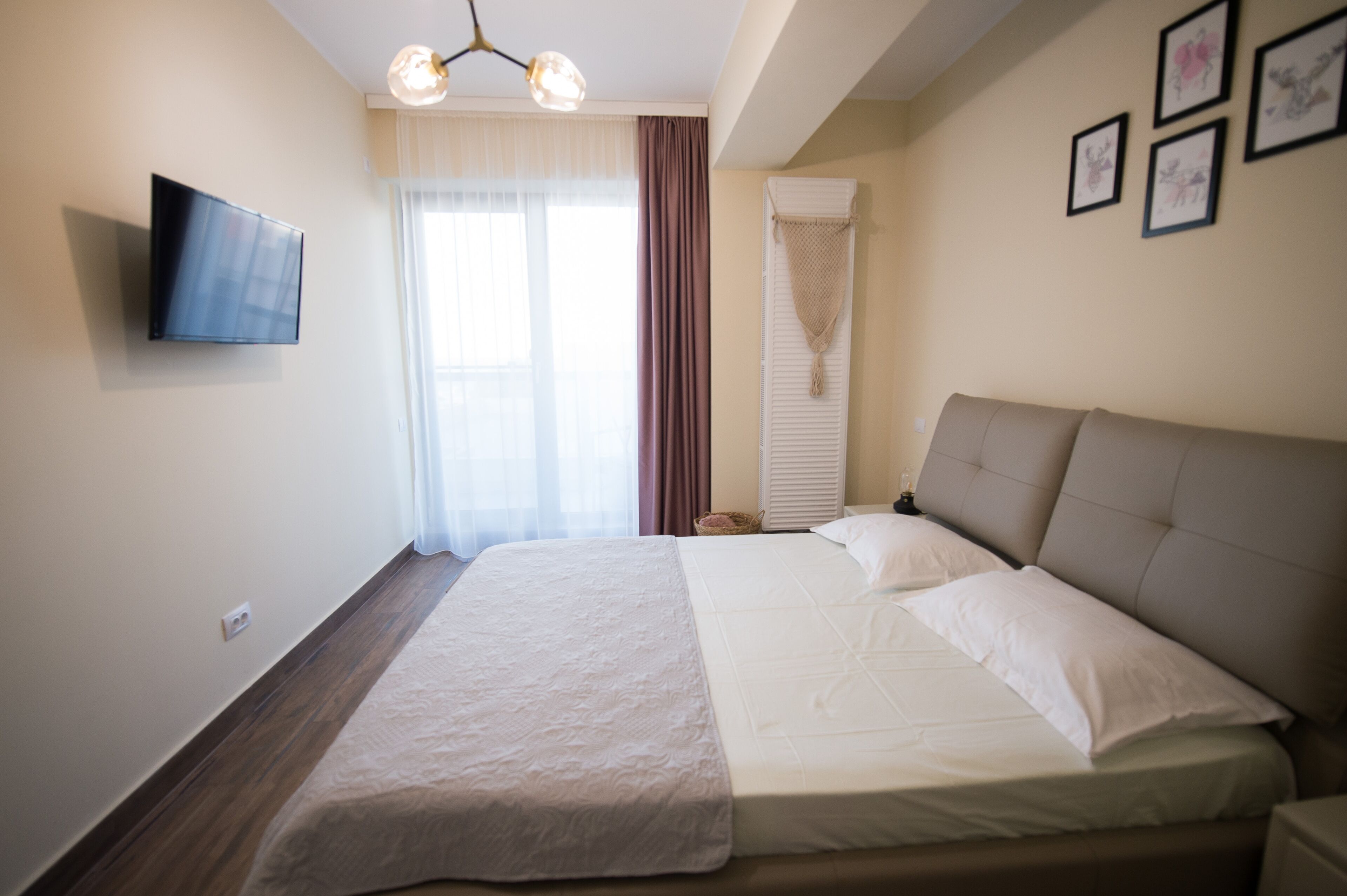A bedroom with a bed, a TV mounted on the wall, and a window with curtains.