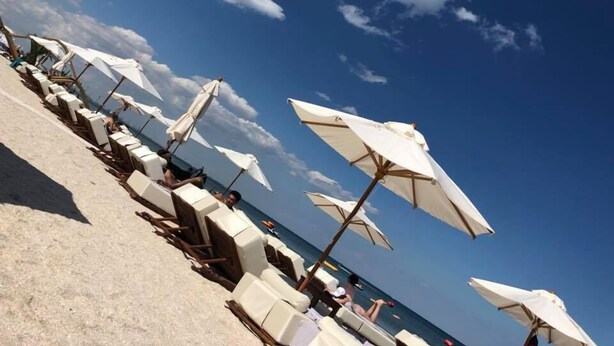 En strand med rader av solstolar och parasoller, en klar himmel och havet i bakgrunden.