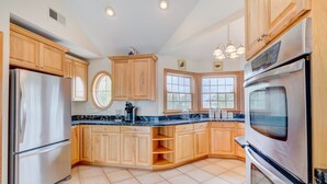 A modern kitchen with wooden cabinets, stainless steel appliances, and a large island. - 1069 - Seadation - Lakeview Corolla Escape w/ Pool & Hot Tub (Corolla)