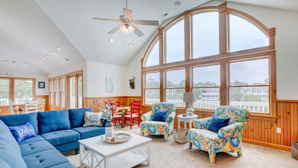 A spacious living room with a large window, a ceiling fan, and a wooden deck visible through the window. - 1069 - Seadation - Lakeview Corolla Escape w/ Pool & Hot Tub (Corolla)