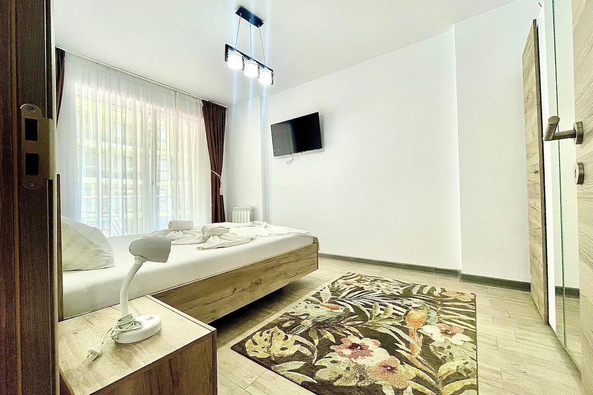 A modern bedroom with a bed, bedside table, lamp, and a flat-screen TV on the wall.