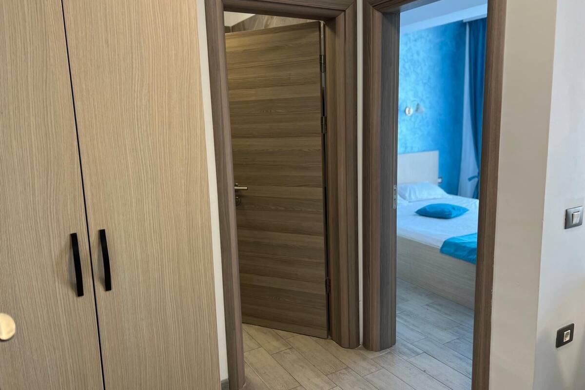 A room with a wooden wardrobe, a bed with blue bedding, and a blue curtain.