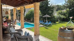 Un patio techado con mobiliario de mimbre, una piscina y vistas al jardín trasero.