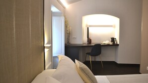 A hotel room with a bed, a desk with a chair, a mirror, and a vase with flowers.