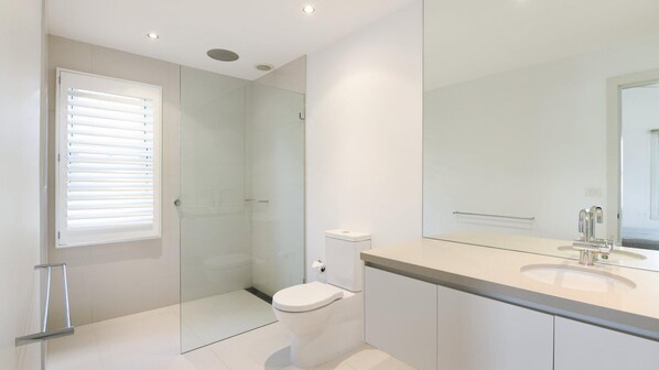 Een moderne badkamer met een douchecabine van glas, een toilet en een wastafelmeubel met een spiegel.