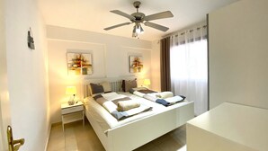 A hotel room with a bed, bedside tables, a ceiling fan, and artwork on the walls. - Ocean Golf & Country Club J&K A3 (Oasis del Sur)