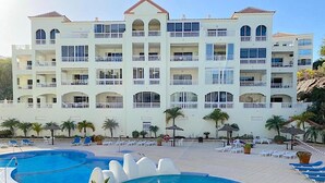 A multi-story hotel with a pool area, outdoor seating, and palm trees. - Ocean Golf & Country Club J&K A3 (Oasis del Sur)