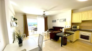 A compact living space with a dining area, a sofa, a kitchen with a microwave, and a ceiling fan. - Ocean Golf & Country Club J&K A3 (Oasis del Sur)