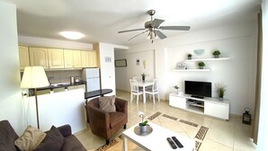 A modern living room with a sofa, a coffee table, a TV stand, and a dining area with chairs and a table. - Ocean Golf & Country Club J&K A3 (Oasis del Sur)