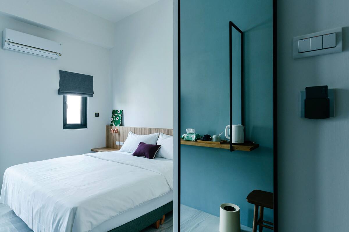 A modern bedroom with a bed, bedside table, and a wall-mounted shelf with a kettle and cups.