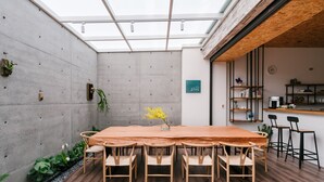 A modern dining area with a wooden table and chairs, a concrete wall, and a skylight. - Sunmiao Inn (Hengchun)