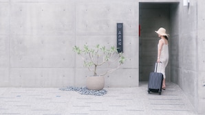 A person with a suitcase standing in front of a concrete wall with a potted plant and a sign. - Sunmiao Inn (Hengchun)