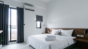 A modern hotel room with a large bed, a wooden headboard, a small bedside table, a nightstand, a potted plant, and a view of the outdoors through a large window. - Sunmiao Inn (Hengchun)