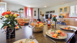 Un coin repas avec une table dressée pour deux personnes, agrémenté d’une nappe à motifs floraux, d’assiettes, de couverts et d’une bouteille de vin.