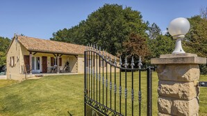 Une maison avec un toit en tuiles, un patio couvert et un portail en pierre.
