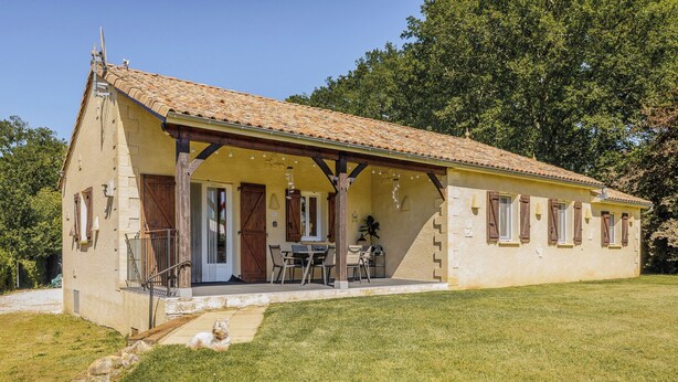 Un bâtiment d’un seul étage, doté d’un toit en tuiles, d’un porche avec des sièges extérieurs et d’une pelouse verdoyante.