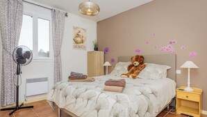 Une chambre à coucher avec un lit, un ours en peluche, un ventilateur et une lampe.