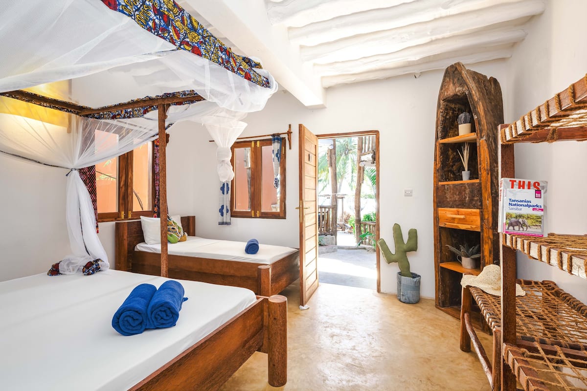 Quarto com uma cama, um banco, uma estante de madeira e um cacto.