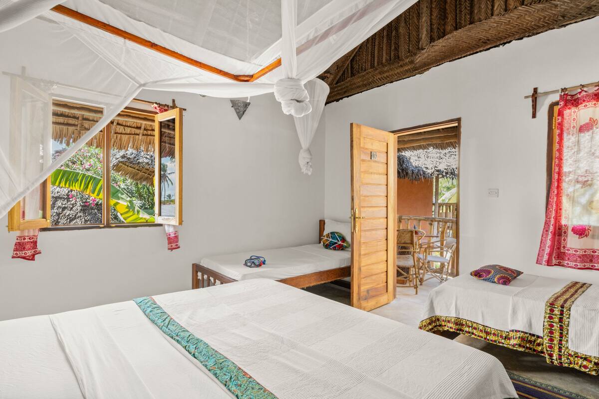 Quarto com duas camas, porta de madeira, janela com vista para o verde e mosquiteiro.