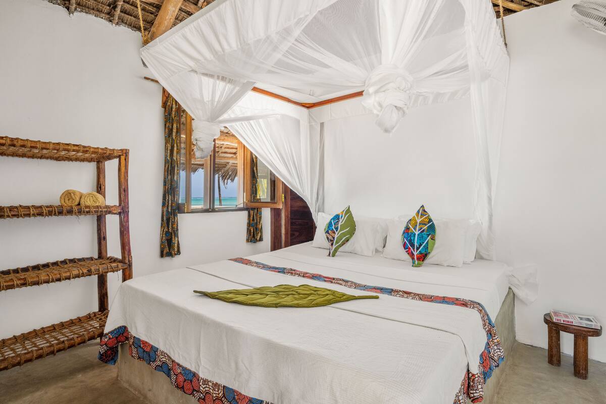 Um quarto com uma cama, um mosquiteiro e uma pequena mesa de madeira.