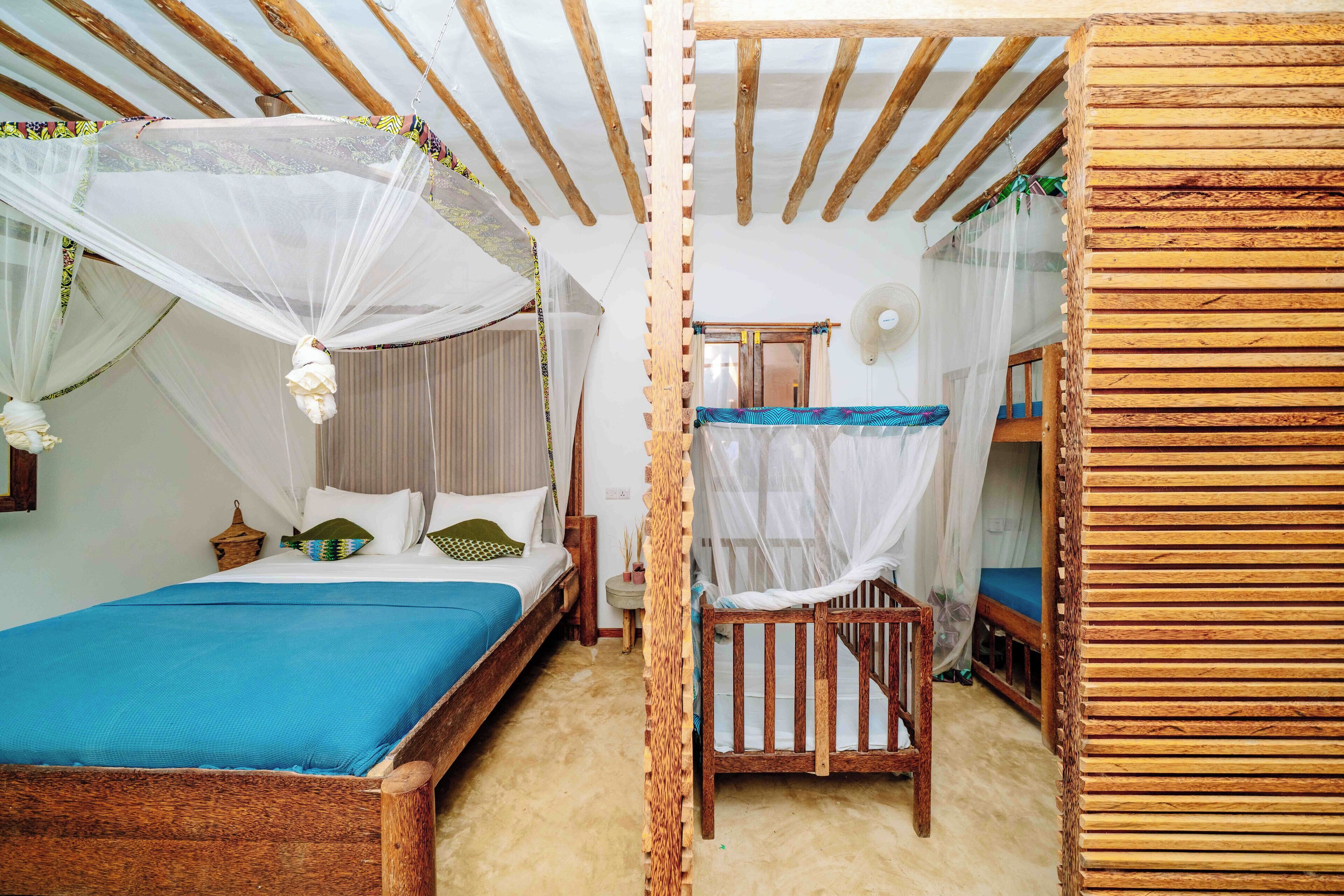 Een kamer met een houten bed, een kleine houten stoel en een stapelbed met muggengaas.