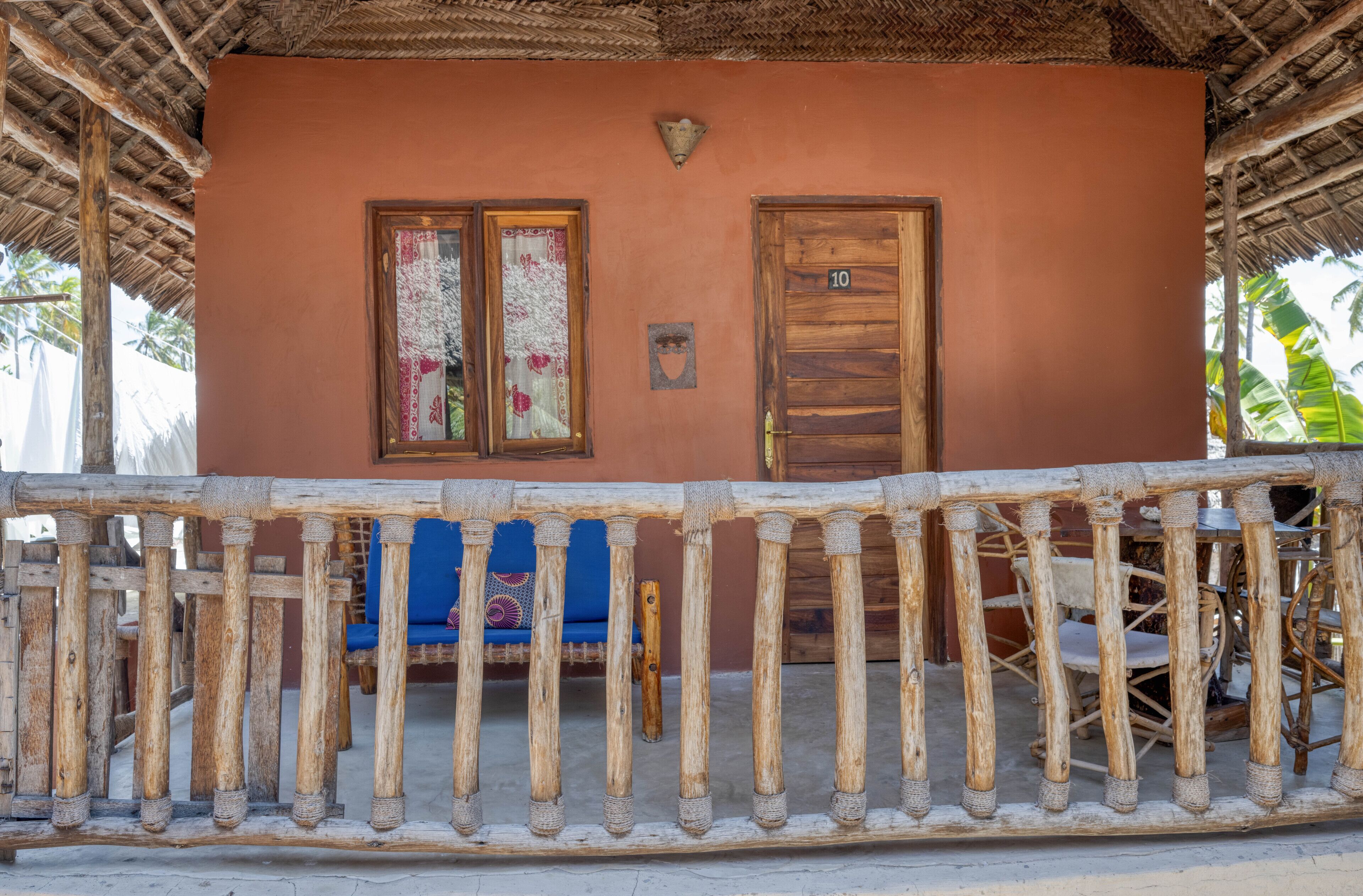 A rustic building with a wooden balcony railing, a blue chair, and a wooden door marked with the number 10.