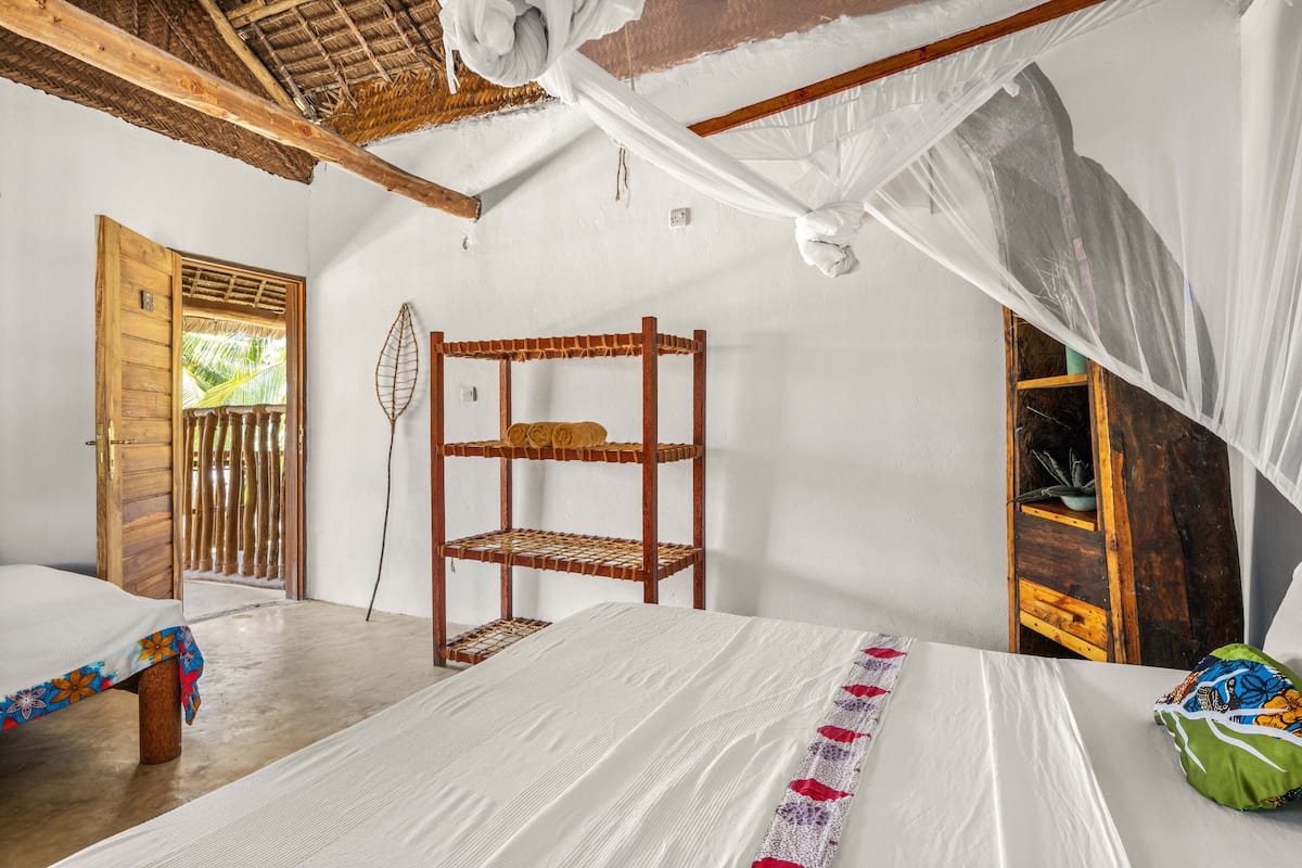 Um quarto com uma cama, uma prateleira de madeira, uma porta e uma janela.